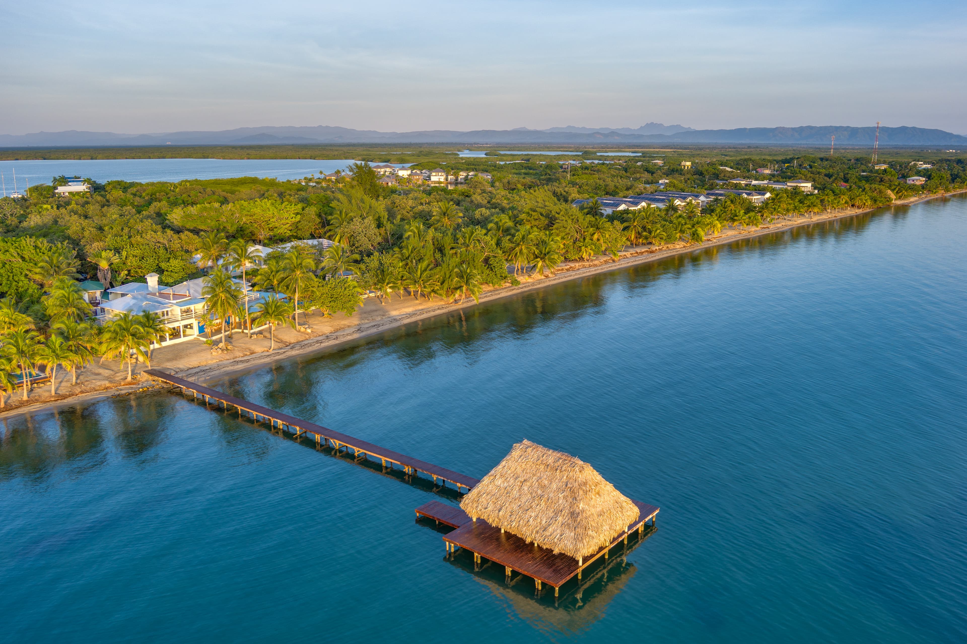 A scenic view of a waterfront with a thatched-roof gazebo extending over calm waters.
