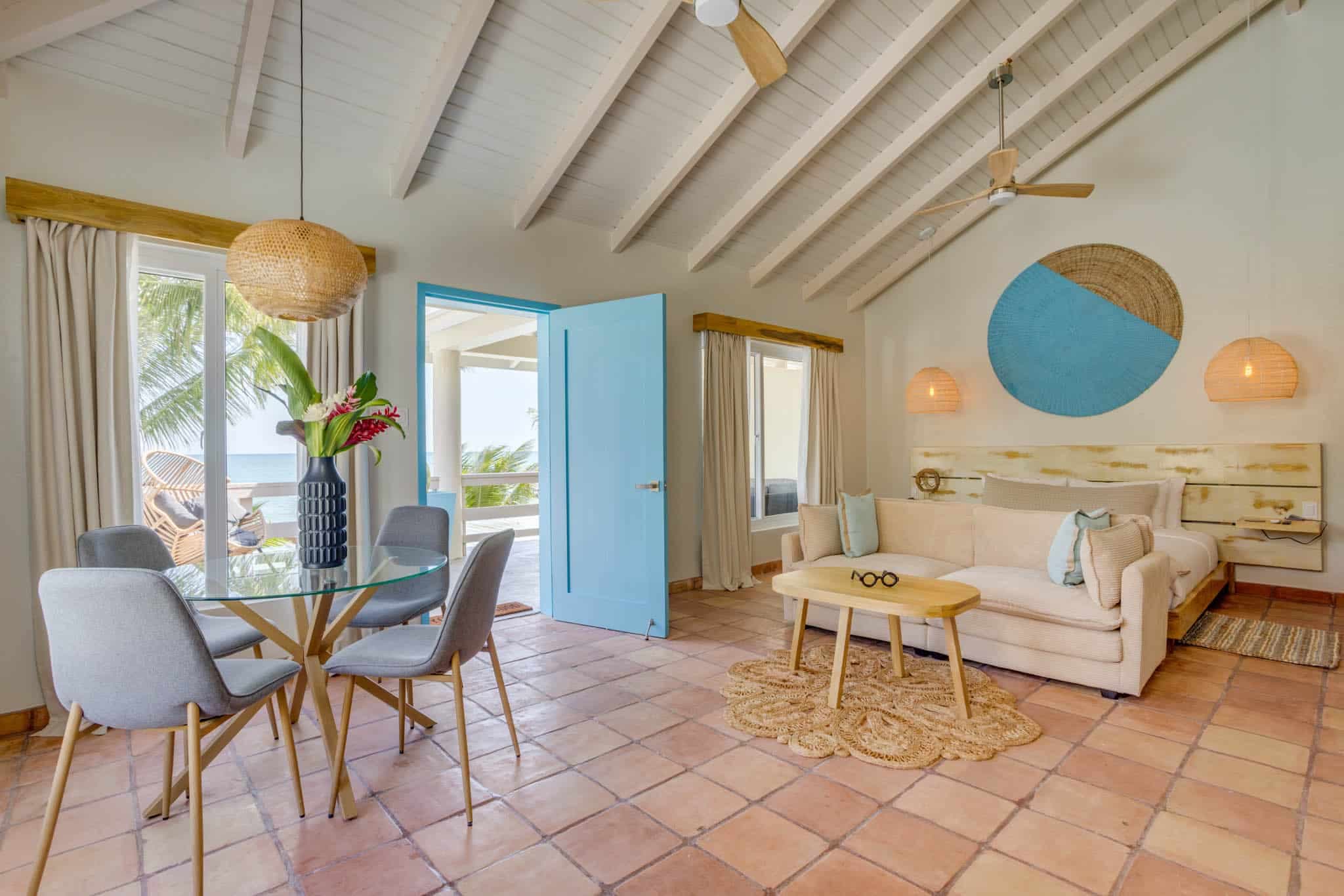 Modern coastal living room with a blue door, dining area, and light-colored furniture.