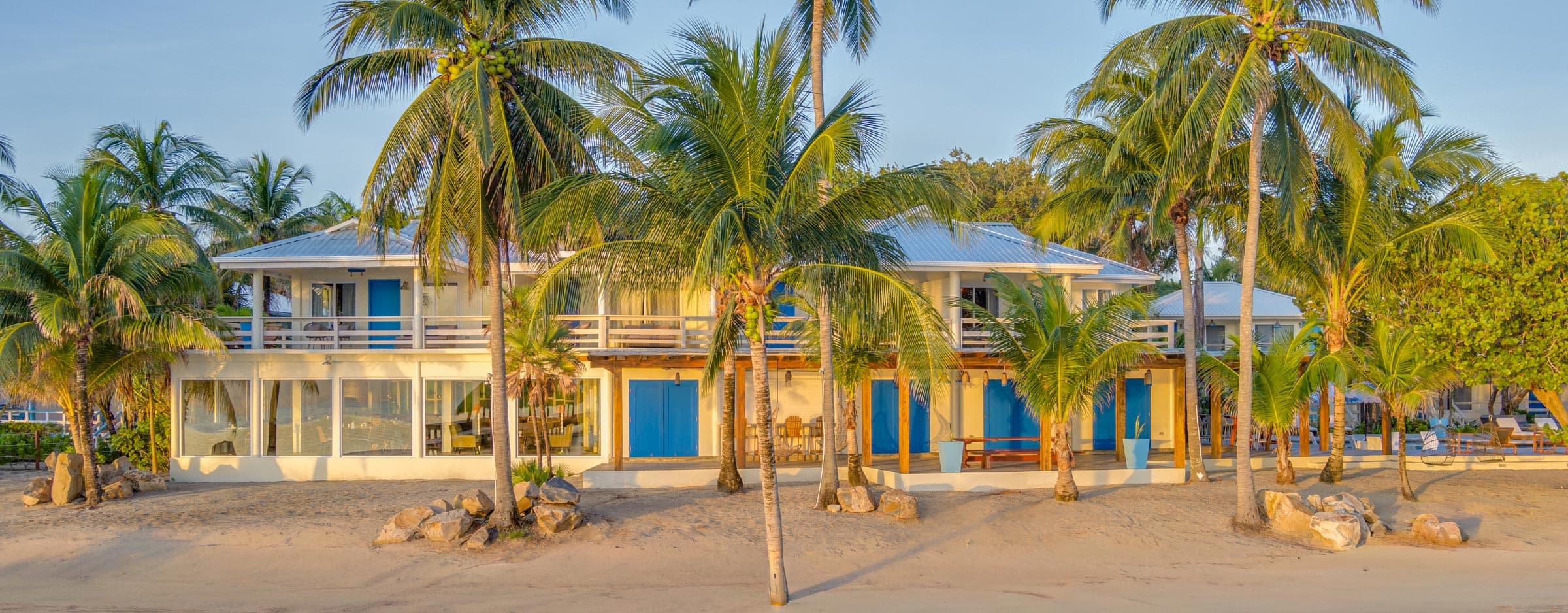 Tropical beachfront property surrounded by palm trees and sandy landscape.