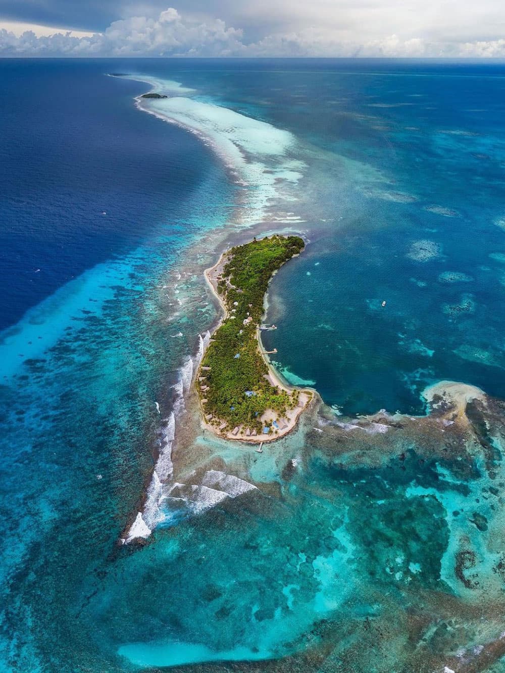 Aerial view of a lush, green island surrounded by vibrant blue waters and a coral reef.