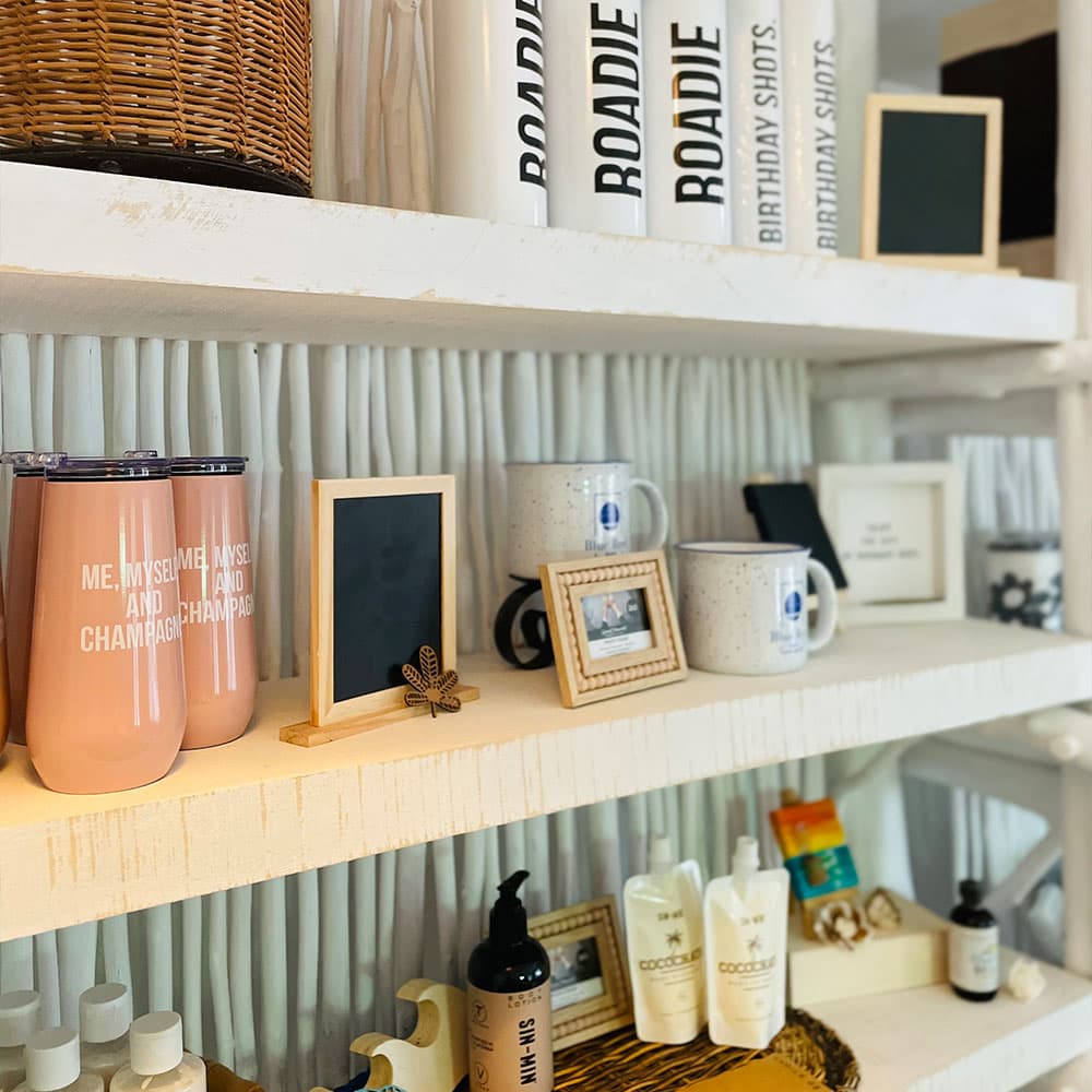 A display of various mugs, decor frames, and skincare products arranged on white shelves.