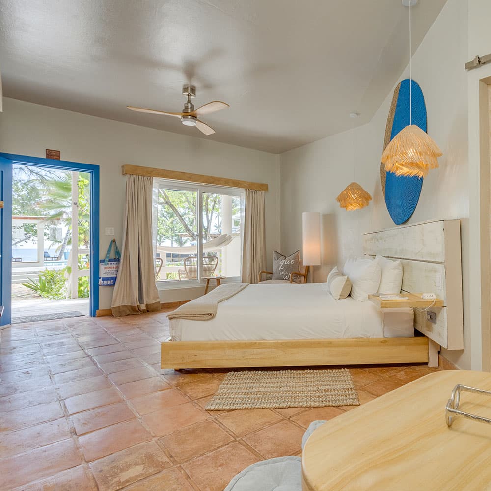 A bright, minimalist hotel room featuring a wooden bed, large window, and contemporary decor.