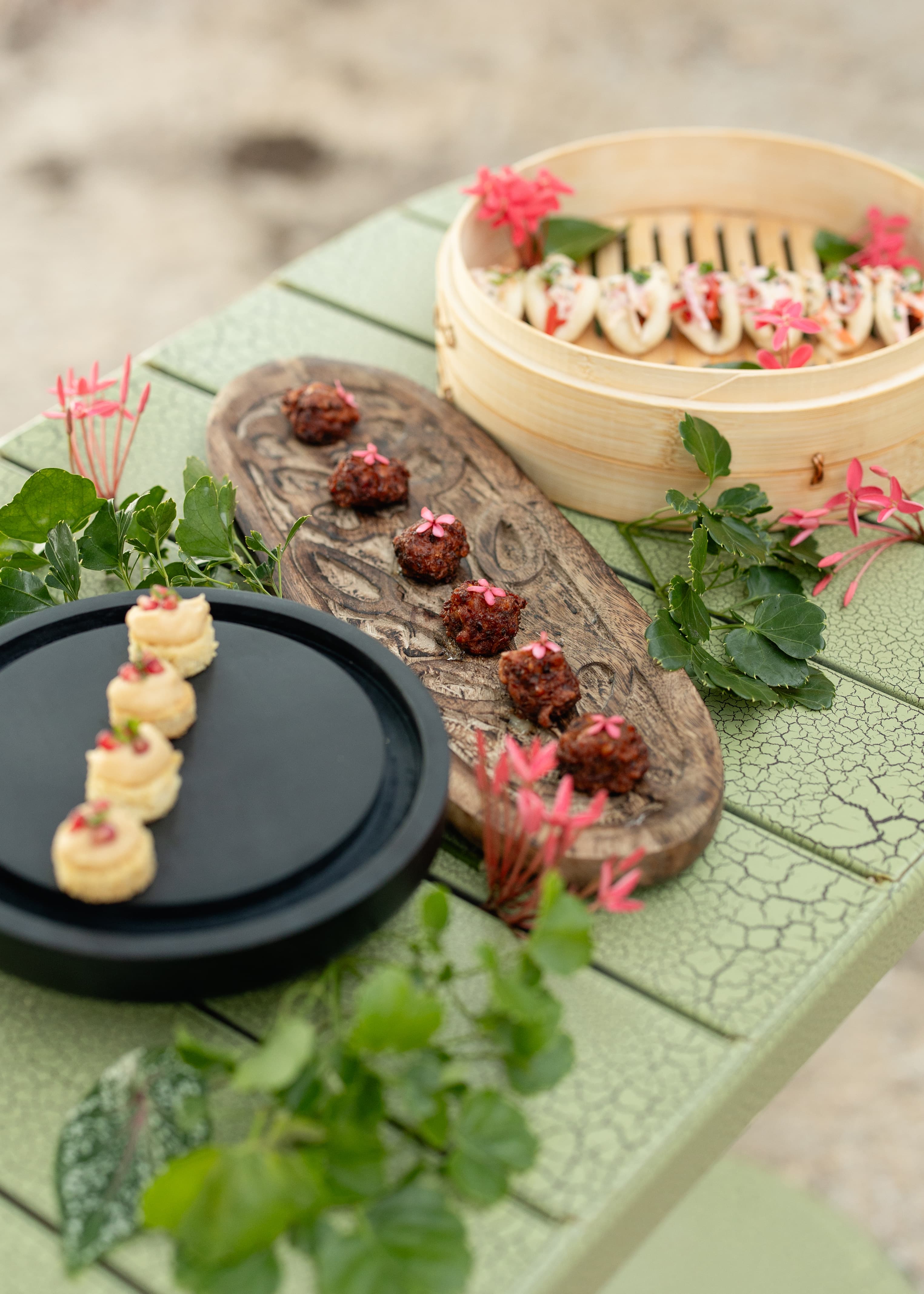 Assorted gourmet appetizers elegantly presented on a textured green table, surrounded by greenery and pink flowers.