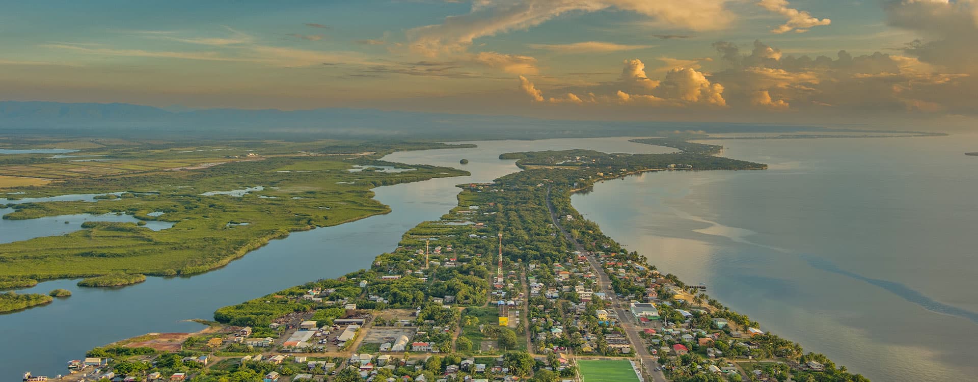 Aerial view of a coastal town bordered by rivers and lush landscapes under a cloudy sky.