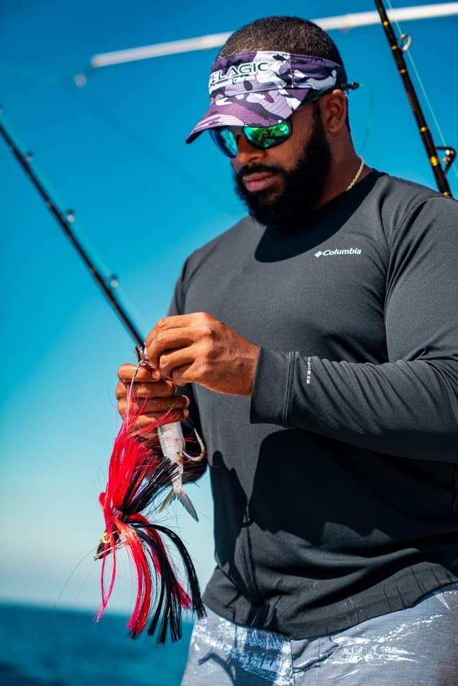 A man in a black long-sleeve shirt prepares fishing tackle on a boat under a clear blue sky.