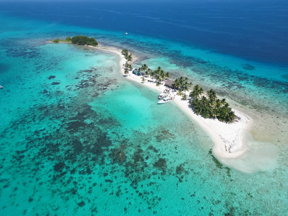 Aerial view of a small tropical island with white sand and palm trees surrounded by turquoise waters.