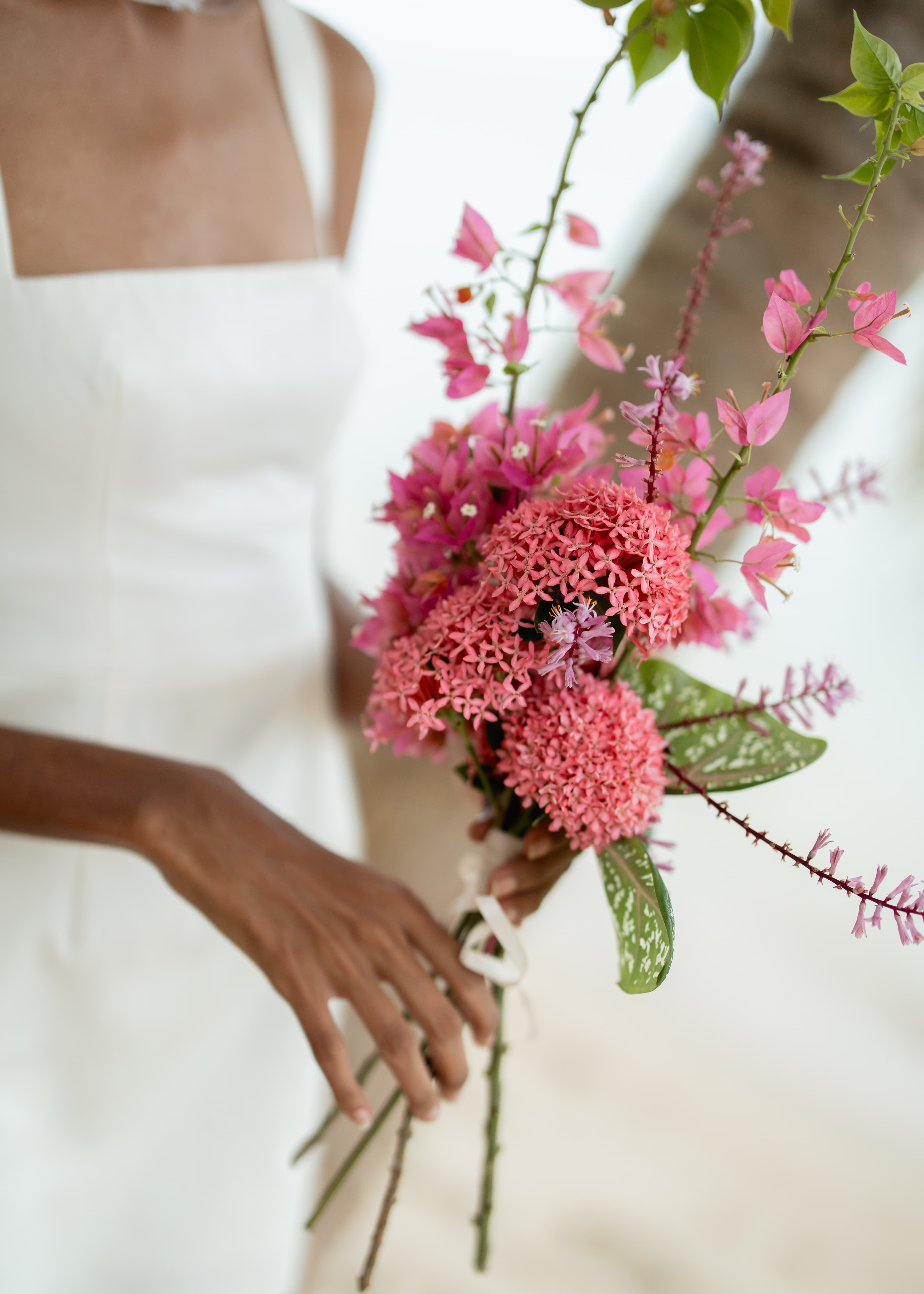A person in a white dress holds a vibrant bouquet of pink flowers.