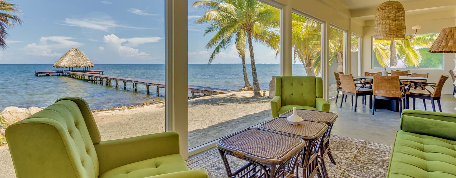 Cozy living area with green chairs overlooking a beach and pier.