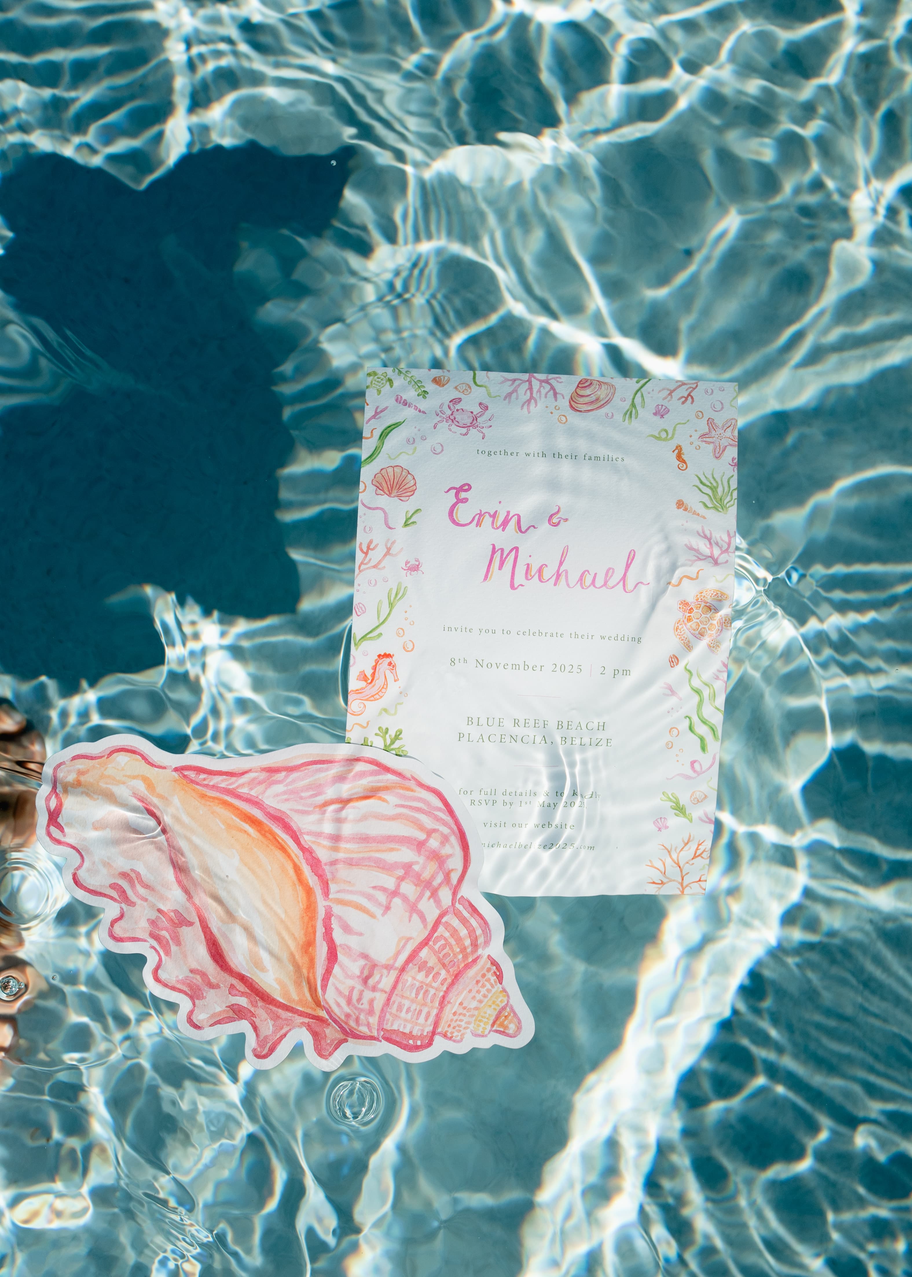 A wedding invitation floats on the surface of a pool, accompanied by a decorative shell.