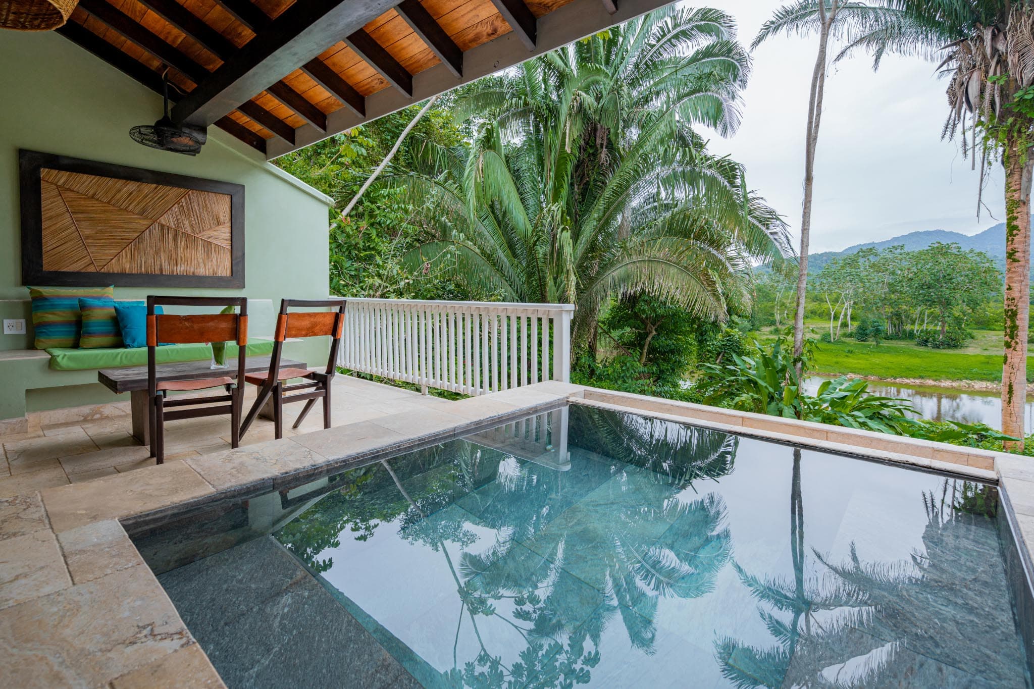 A modern outdoor space featuring a small pool, dining area, and lush tropical surroundings.
