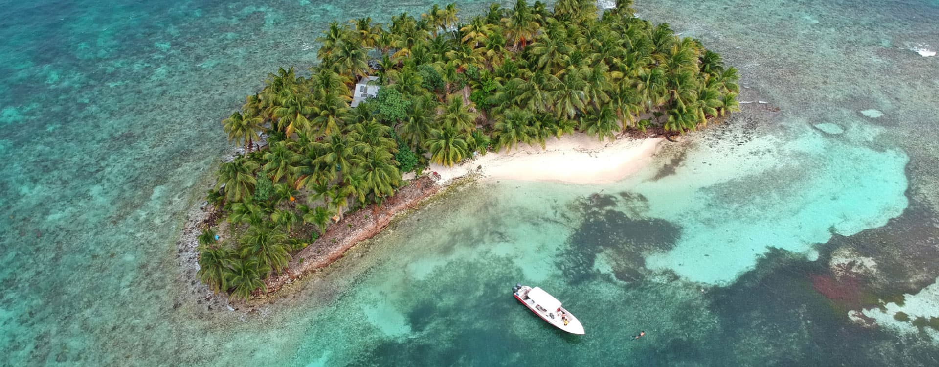 Aerial view of a small tropical island with lush greenery and a boat anchored nearby.