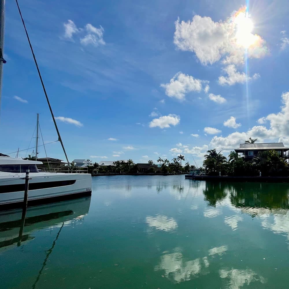 A sailboat is moored in a tranquil lagoon under a bright blue sky with fluffy clouds.