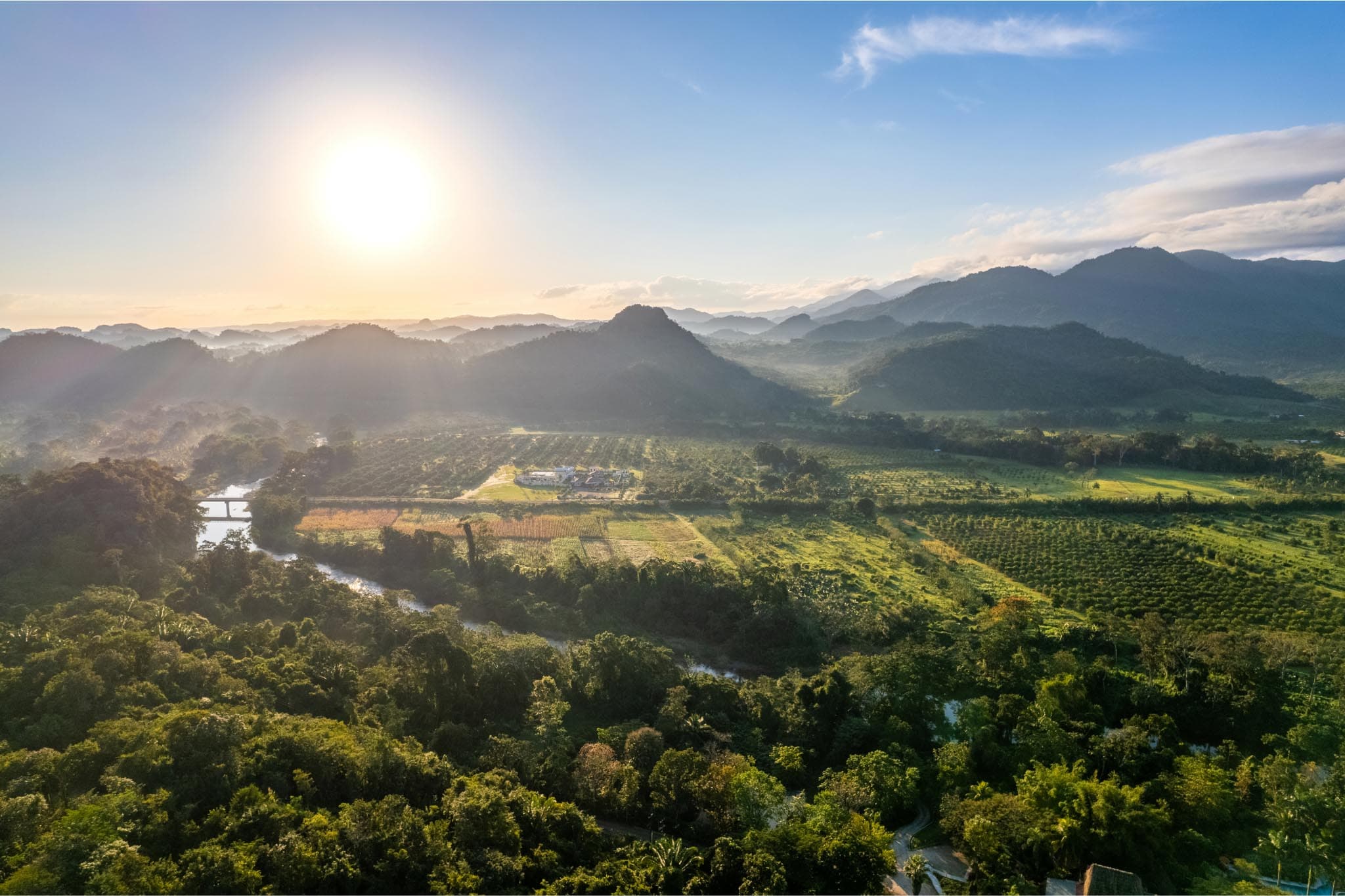 Aerial view of lush green hills and fields under a bright sunrise.