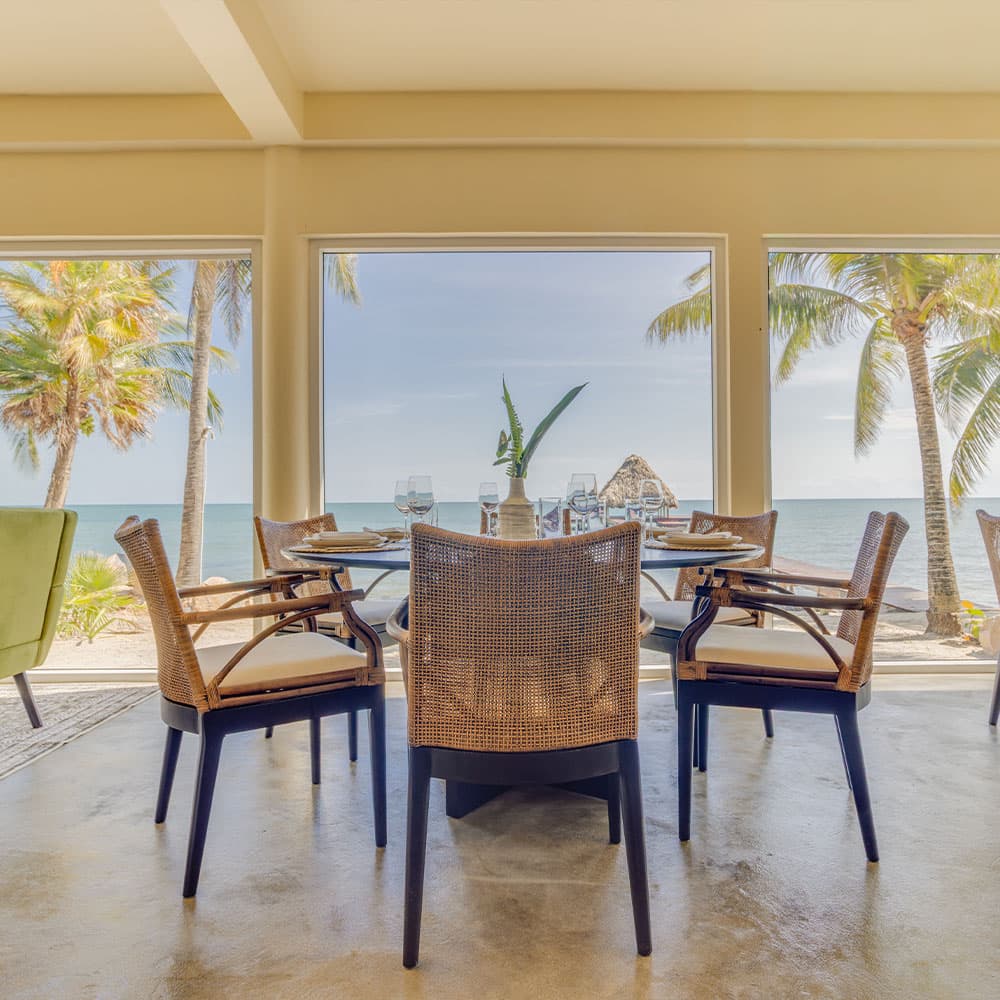 A dining area with wicker chairs offers a view of palm trees and the ocean.