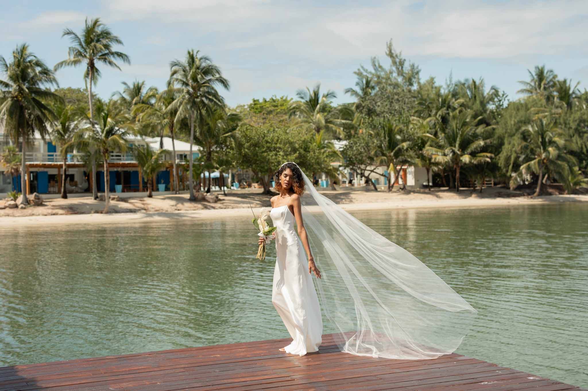 A woman in a wedding dress standing on the pier at Blue Reef Beach in Placencia A woman in a wedding dress standing on the pier at Blue Reef Beach in Placencia